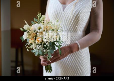 Unrecognizable woman in lace wedding dress holding a beautiful green bouquet with white and yellow roses on a blurred background Stock Photo