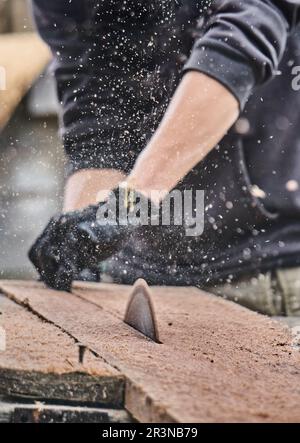 High angle of crop anonymous male carpenter in casual clothes and gloves sawing planks of wood with aged sawing machine during work in community of Ot Stock Photo