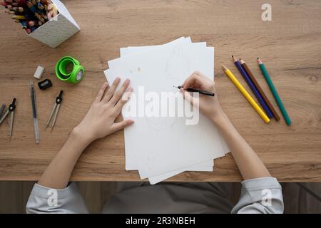Top view of crop anonymous female designer drawing on white paper sheet with colorful pencils while sitting at wooden table Stock Photo