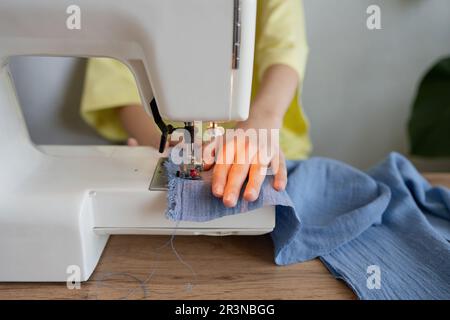 Anonymous young seamstress sewing on the sewing machine as they prepare to create a new design project in a light studio Stock Photo