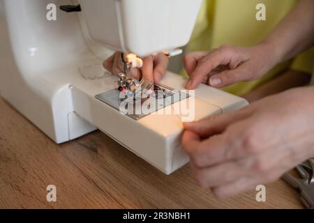 Anonymous female dressmakers putting thread into sewing machine while preparing for creating new design project in light atelier Stock Photo
