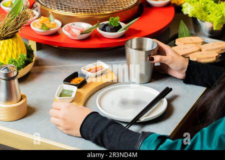 Young Asian man eating Korean Barbecue buffet ordering menu while grilling beef in the restaurant. Stock Photo