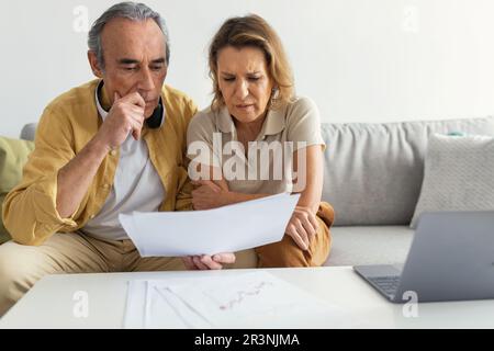 Upset married senior spouses looking at loan documents, checking financial papers and planning budget at home Stock Photo