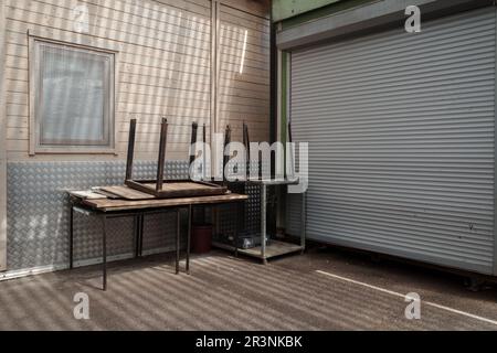 Exterior view in front of closed storefront, stack of stall tables, and closed roller shutter door, at the closed market. Stock Photo
