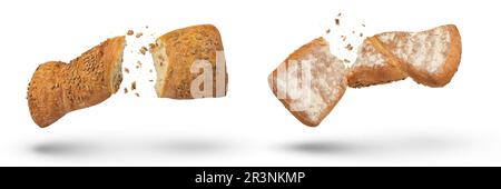 Two loaves of crispy bread isolated on white. Loaves of freshly baked crispy bread are broken in half with crumbs flying in all directions at the Stock Photo
