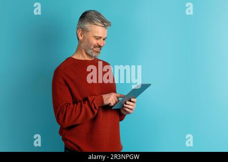 Joyful middle aged man using digital tablet on blue Stock Photo