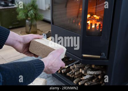 Hands kindle the hearth with economical briquettes. Fuel briquettes made of pressed sawdust for kindling the furnace - economica Stock Photo