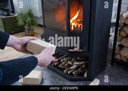 Hands kindle the hearth with economical briquettes. Fuel briquettes made of pressed sawdust for kindling the furnace - economica Stock Photo