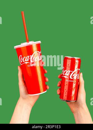 Berlin Germany May 23 2023 Hands holding Cola drinks in red take-away paper mug with straw and metal can, tin. Stock Photo