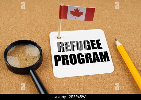 On the table is the flag of Canada, a pencil, a magnifying glass and a sheet of paper with the inscription - Refugee Program Stock Photo