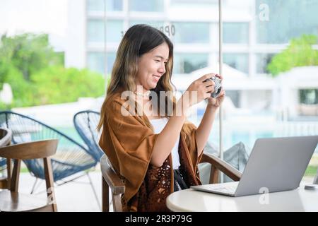 Asian woman using digital camera and laptop at coffee shop Stock Photo