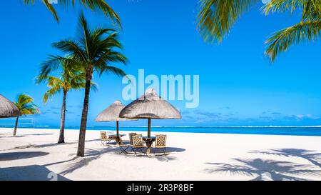 Tropical beach with palm trees and white sand blue ocean and beach beds with umbrella,Sun chairs and parasol under a palm tree a Stock Photo