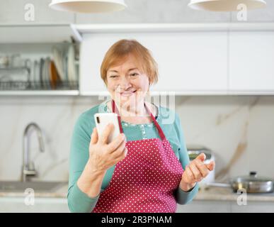 Smiling older woman sending messages using smartphone with someone on her phone Stock Photo