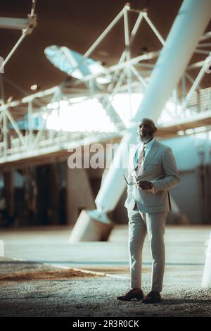 Vertical shot of a stylish bald business black man, with a long beard with white hair, dressed in a suit, holds a pair of sunglasses with a pensive ex Stock Photo