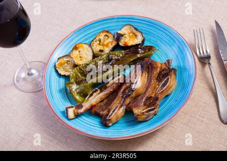 on blue plate-grilled beef ribs with fried vegetables-aubergine, pepper,onion.Spanish dish-churrasco Stock Photo