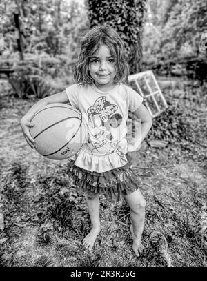 Little girl posing for the camera outside with a basketball. (Black and White Photo) (NC State, 2023) Stock Photo