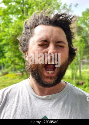 A man's face getting hit by wind, his eyes closed and mouth open Stock Photo