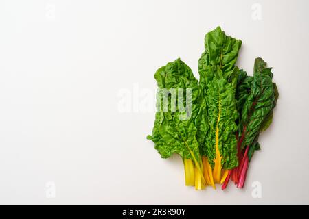 Bunch of rainbow swiss chard leaves on beige stone table. Top view of yellow, orange, red and green fresh swiss chards. Stock Photo