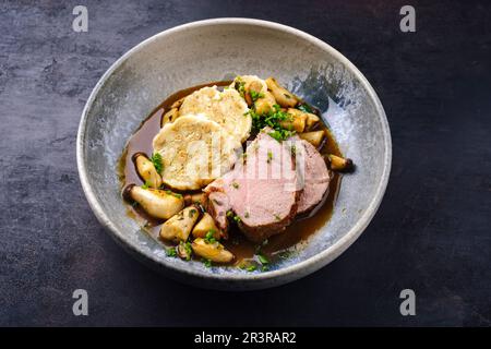 Traditional German pork roast served with bread dumpling and king oyster mushroom in dark beer sauce served as close-up in a Nor Stock Photo