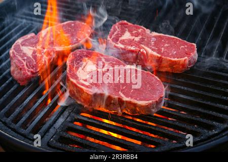 Barbecue dry aged angus rib-eye beef steak grilled as close-up on a charcoal grill with fire and smoke Stock Photo
