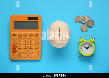 Piggy bank, alarm clock, calculator and coins on light blue background, flat lay Stock Photo
