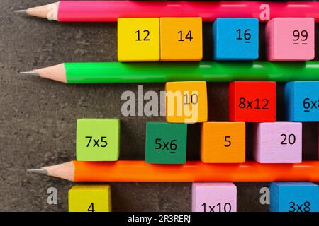 Many colorful cubes with numbers, multiplications and pencils on dark grey table, flat lay Stock Photo