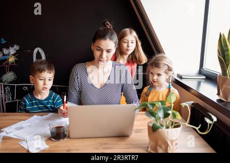 Brunette mother, daughter and son using a laptop, while mom drinking breakfast coffee Stock Photo