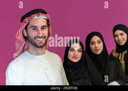 Group portrait of young Muslim people Arabian men with three Muslim women in a fashionable dress with hijab isolated on a pink b Stock Photo