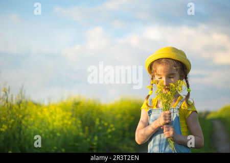 A girl in a yellow summer field sniffs a bouquet of flowers. Sunny day, holidays, allergy to flowering, freedom. Cultivation of Stock Photo