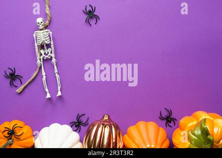 Halloween layout of garland of skeleton on a rope, glowing Jack o Lantern, pumpkins, spiders on a purple background. Flat lay ho Stock Photo