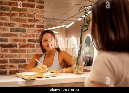 Female receptionist working in beauty salon and writing down appointment of woman customer Stock Photo