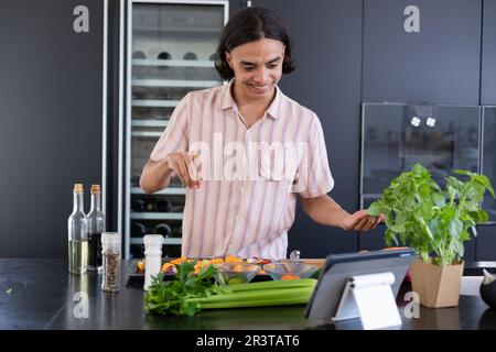 Happy biracial man cooking and using tablet in kitchen Stock Photo