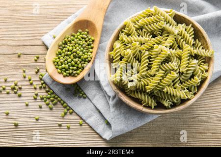 Mung bean fusilli pasta on a old wooden background. Bowl with raw pasta and green mung bean. Gluten free pasta. Stock Photo