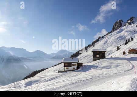 Swiss chalets on the Alps with ski slopes in winter sprorts resort with morning fog and mist rising up the valley Stock Photo