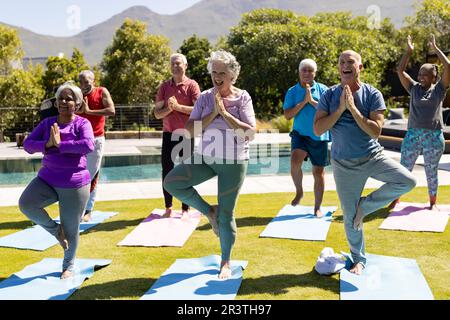 Happy diverse senior friends practicing yoga standing in sunny garden Stock Photo