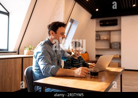Brunette father and son using a laptop while father drinking breakfast coffee Stock Photo