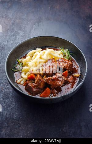 Traditional Hungarian braised venison goulash with vegetable and spaetzle in spicy sauce served as close-up in a Nordic design b Stock Photo