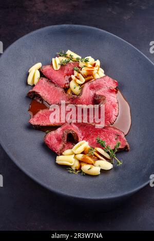 Traditional Italian chianina sliced roast beef with gnocchetti sardi pasta in spicy red wine sauce served as close-up in a desig Stock Photo