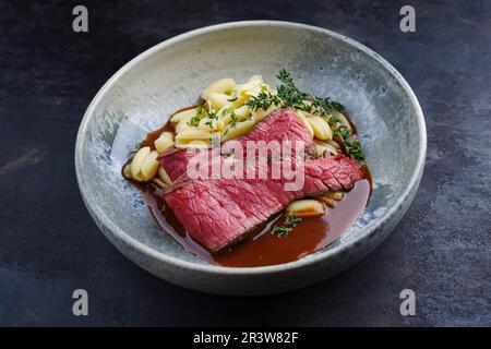 Traditional Italian chianina sliced roast beef with gnocchetti sardi pasta in spicy red wine sauce served as close-up in a Nordi Stock Photo