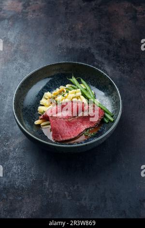 Traditional Italian chianina sliced roast beef with gnocchetti sardi pasta and beans in spicy red wine sauce served as close-up Stock Photo