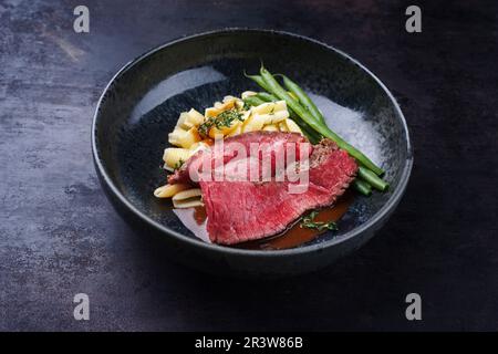 Traditional Italian chianina sliced roast beef with gnocchetti sardi pasta and beans in spicy red wine sauce served as close-up Stock Photo