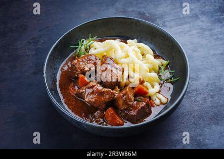 Traditional Hungarian braised venison goulash with vegetable and spaetzle in spicy sauce served as close-up in a Nordic design b Stock Photo