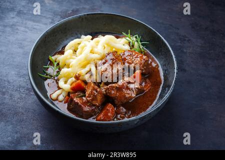 Traditional Hungarian braised venison goulash with vegetable and spaetzle in spicy sauce served as close-up in a Nordic design b Stock Photo