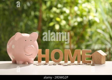 Piggy bank, word Home, house model and coins on table outdoors. Saving money concept Stock Photo