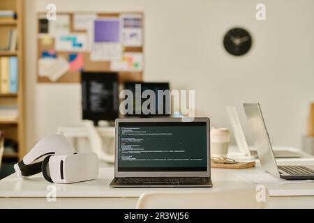 Laptop with program code on screen on table in IT office Stock Photo