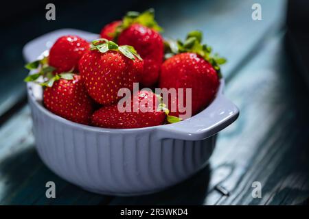 A single lilac Bowl of fresh strawberries on blue wooden board in dramatic light. minimal scene Stock Photo