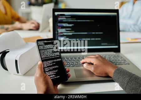 Close-up of man writing security codes on gadgets and connecting smartphone to laptop sitting at his workplace Stock Photo