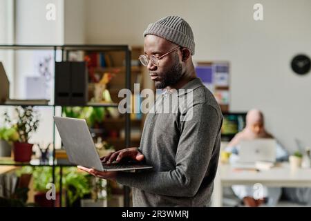 African American developer typing on laptop while standing in IT office Stock Photo