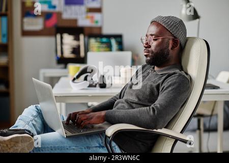 African American developer working with software on laptop while sitting on chair in office Stock Photo