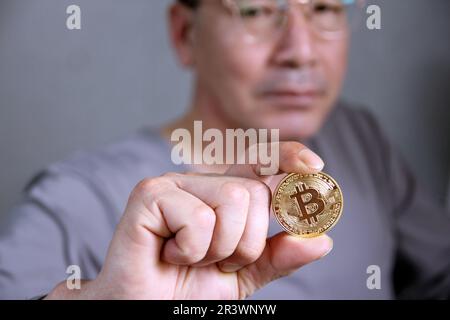 Hand hold gold bitcoin cryptocurrency on grey background. Physical bit coin. Digital currency Stock Photo